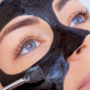 The procedure for applying a black mask to the face of a beautiful woman.